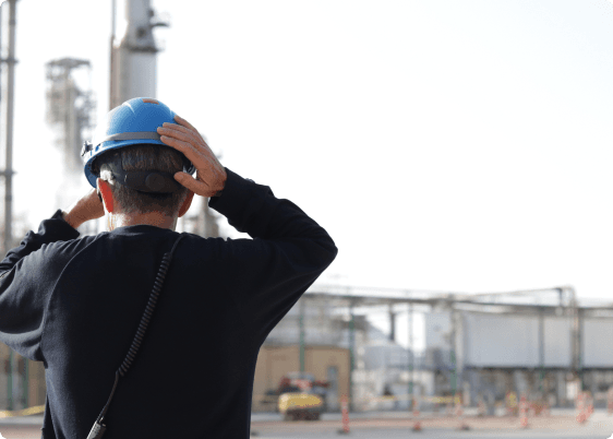 A man puts on a blue hard hat as he walks toward the facility